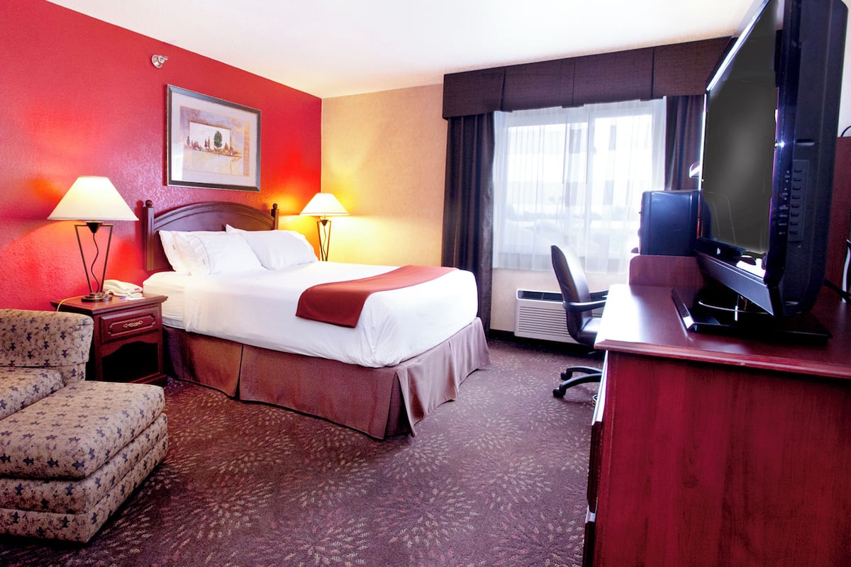 A hotel room with a bed, bedside lamps, a desk with a television, a chair, and a picture on the wall.