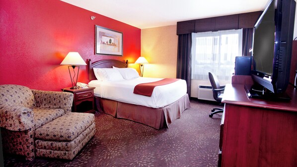 Habitación de hotel con cama, lámparas de noche, escritorio con televisor, silla e imagen en la pared.