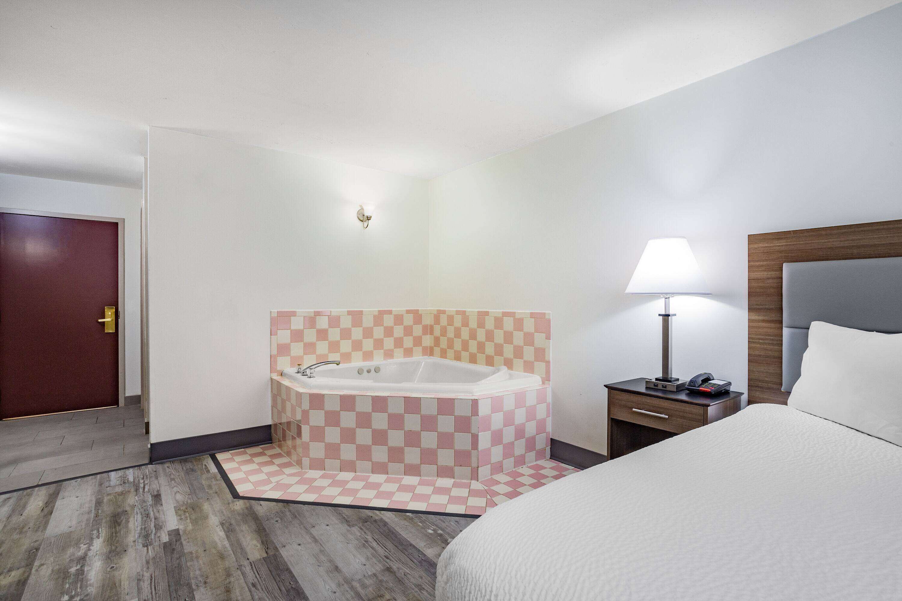 Ein Hotelzimmer mit Schachbrettmuster-Boden, einem großen Bett, einem Nachttisch mit Lampe und einem Badezimmer mit Schachbrettmuster-Wand und einer Badewanne.