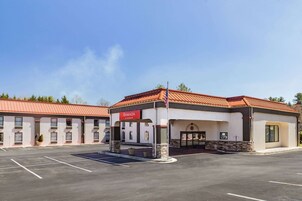 Un hotel Ramada con techo rojo, estacionamiento y cielo azul despejado.