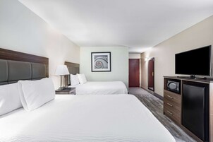 Habitación de hotel con dos camas, un televisor, un microondas y un cuadro enmarcado en la pared.