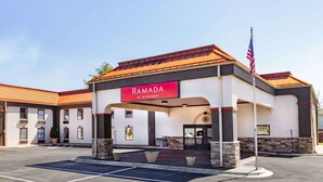 Entrada de un hotel con un letrero que dice "RAMADA BY WYNDHAM", un estacionamiento y una bandera estadounidense.