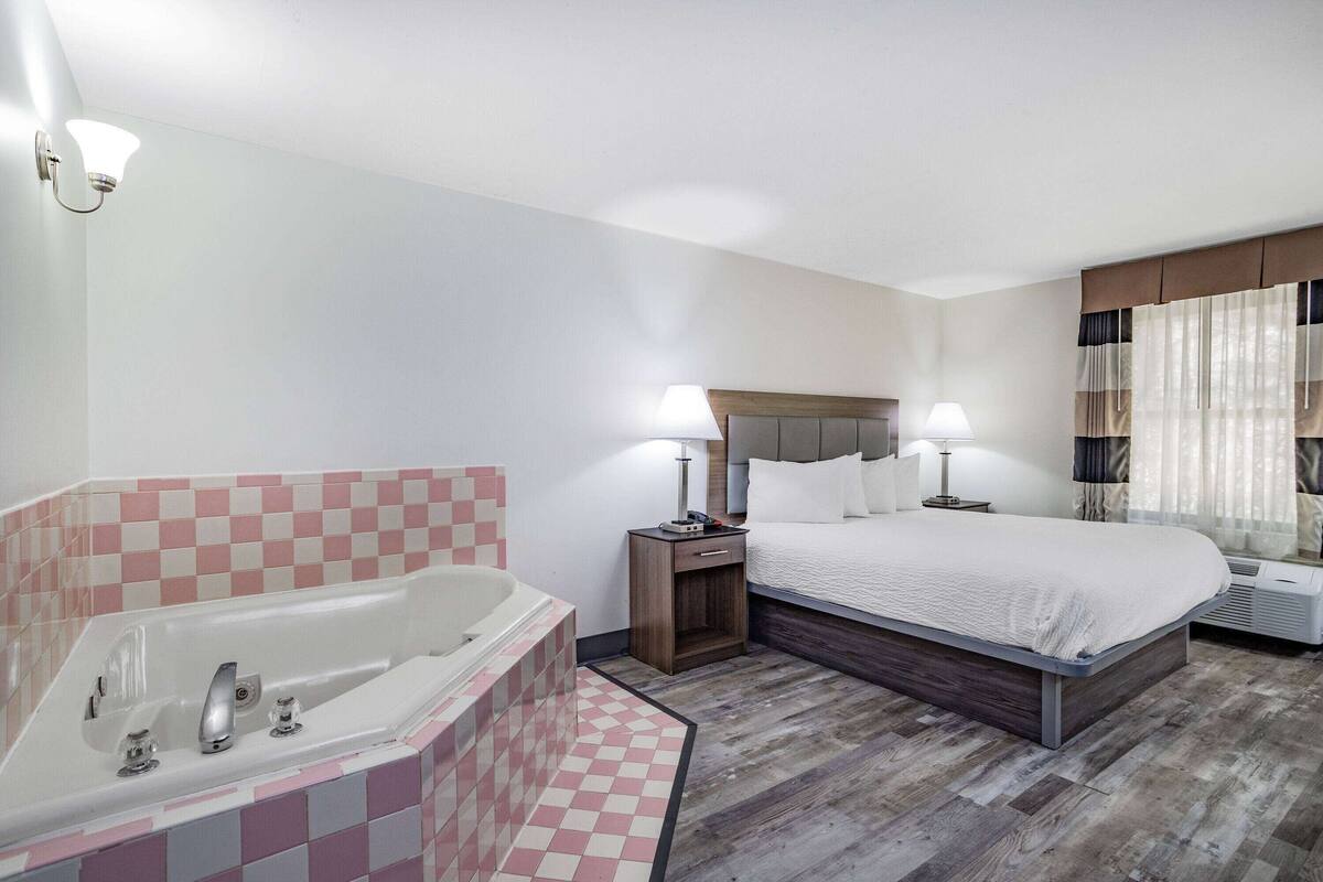 Habitación de hotel con una cama grande, baño privado con bañera y ventana con cortinas.