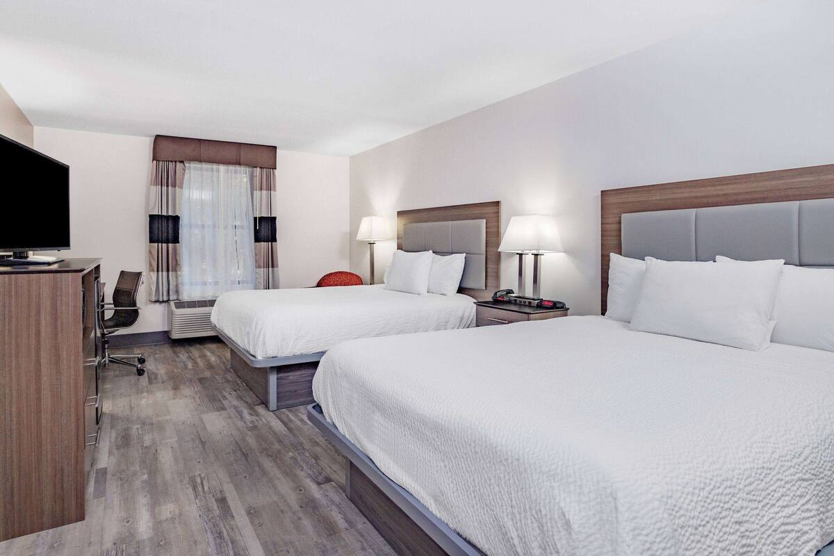 Habitación de hotel con dos camas, un escritorio con computadora, un televisor y una ventana con cortinas.