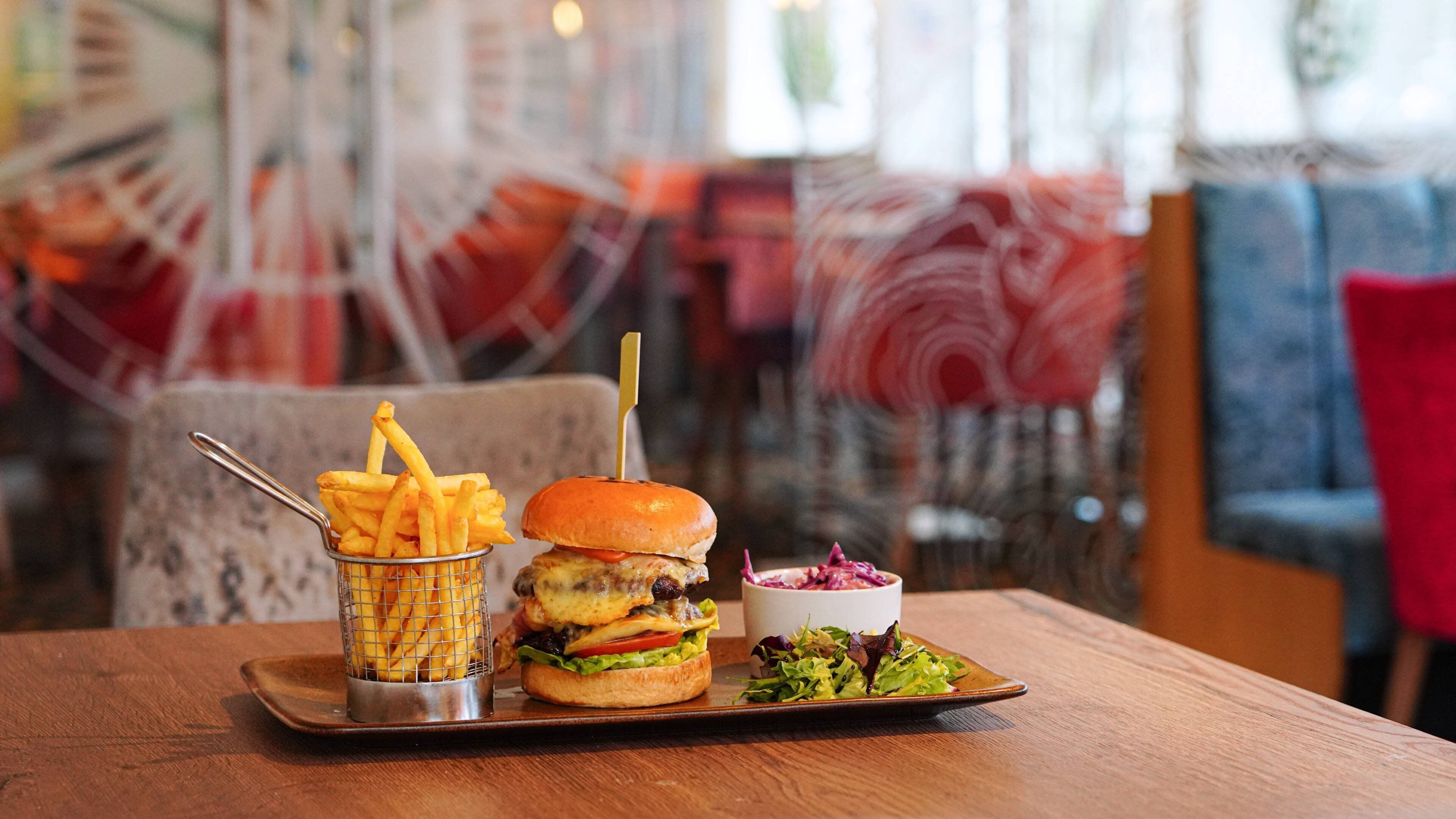 A meal consisting of a burger, fries, and a salad on a wooden table in a restaurant.