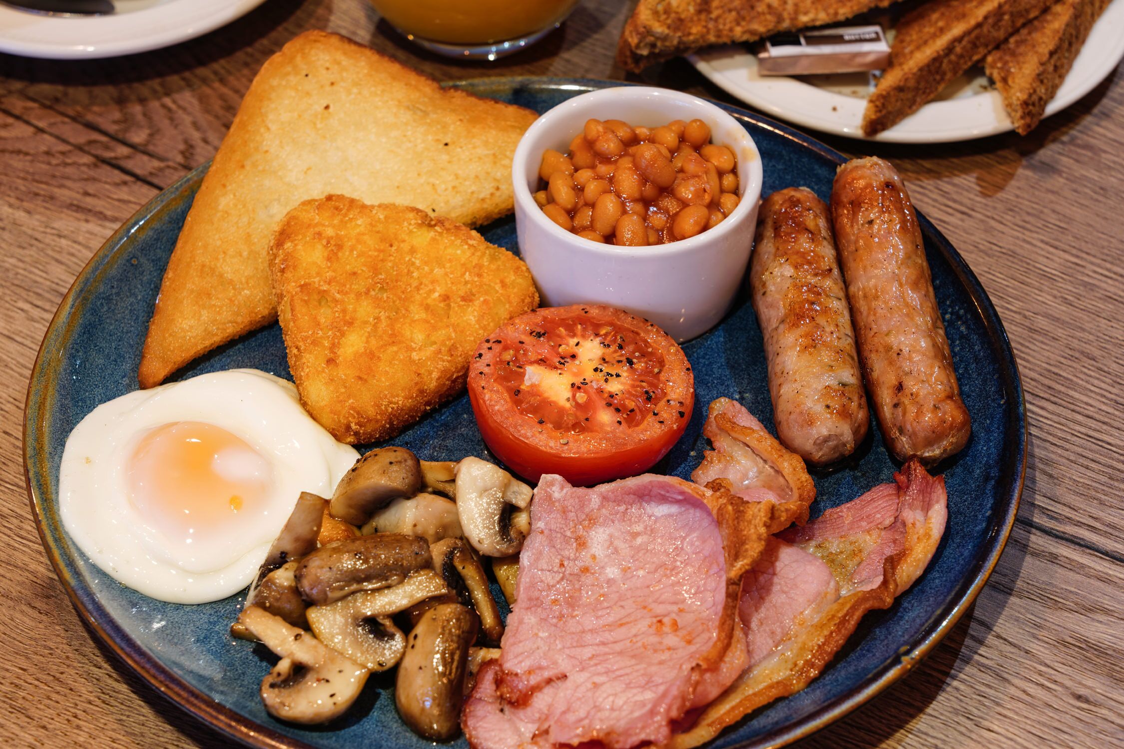 Ein Frühstücksteller mit Toast, Bohnen, Würstchen, einem Spiegelei, Tomate, Pilzen und Speck.