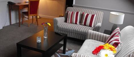 A living room with striped sofas, a dark coffee table, a lamp, and a desk with a chair.