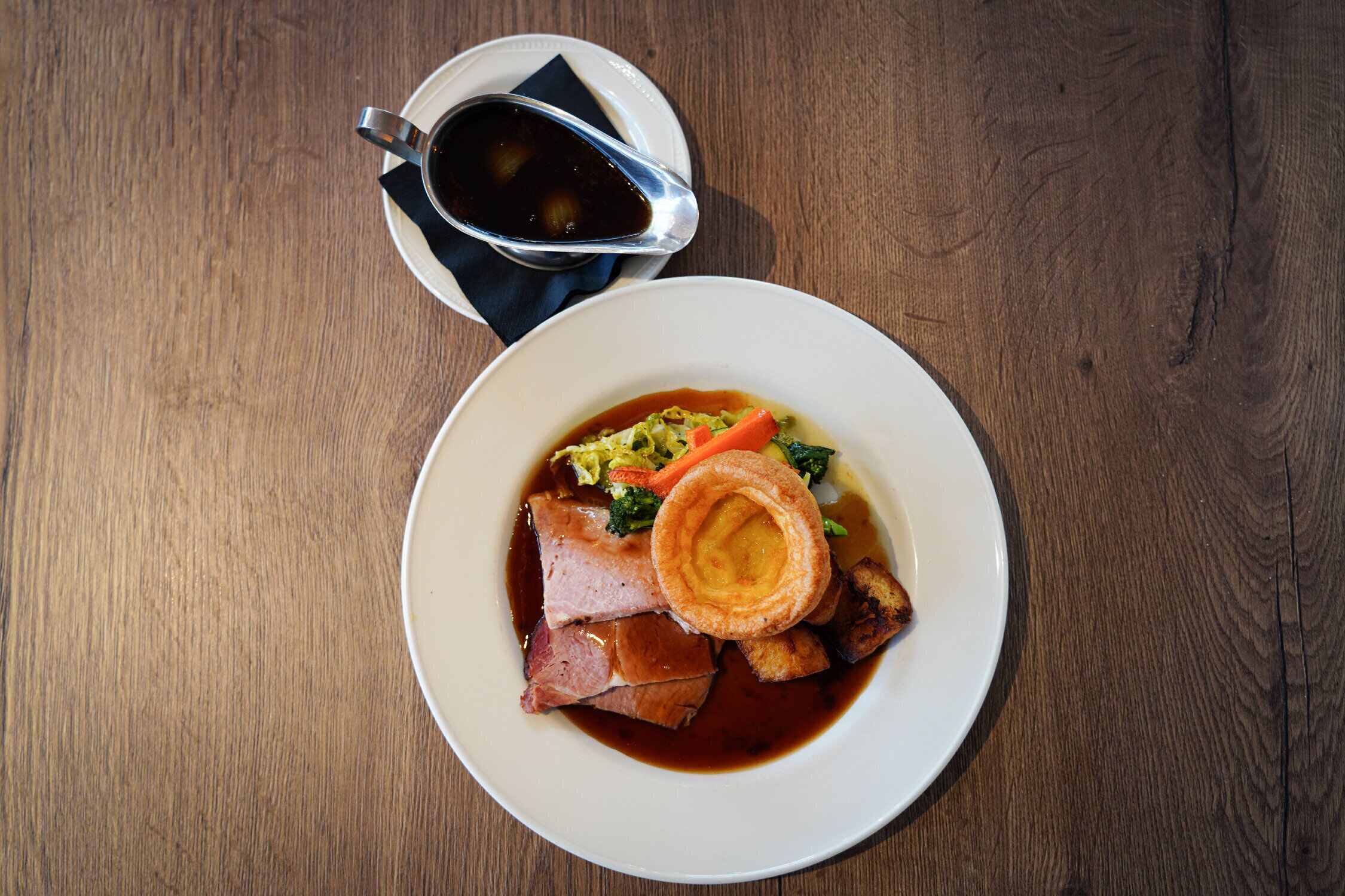 A plate of food with roast beef, Yorkshire pudding, vegetables, and gravy.