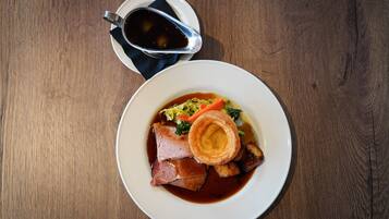 A plate of food with roast beef, Yorkshire pudding, vegetables, and gravy.