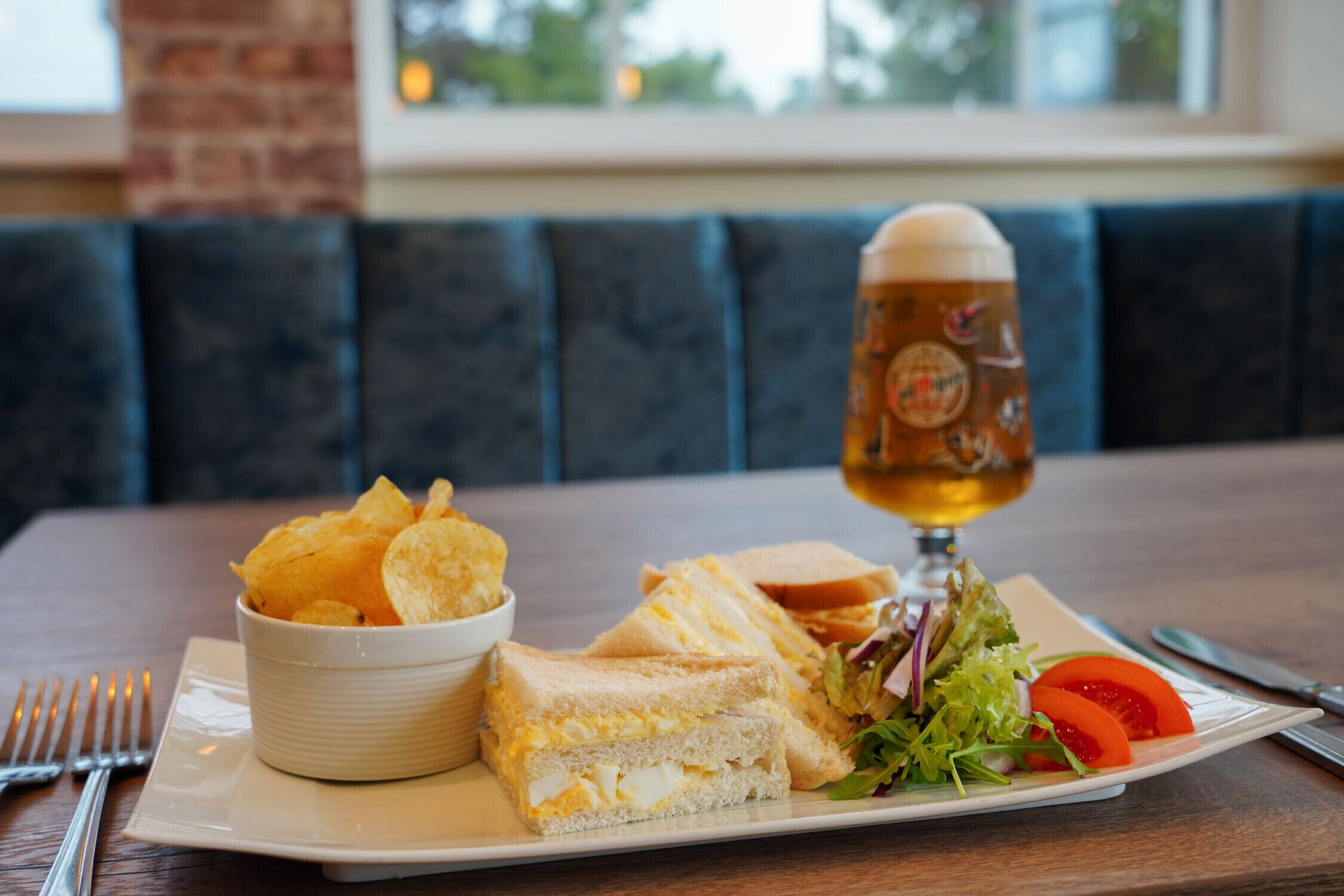Un pasto composto da panini, patatine e un'insalata su un piatto, con un bicchiere di birra sul tavolo.