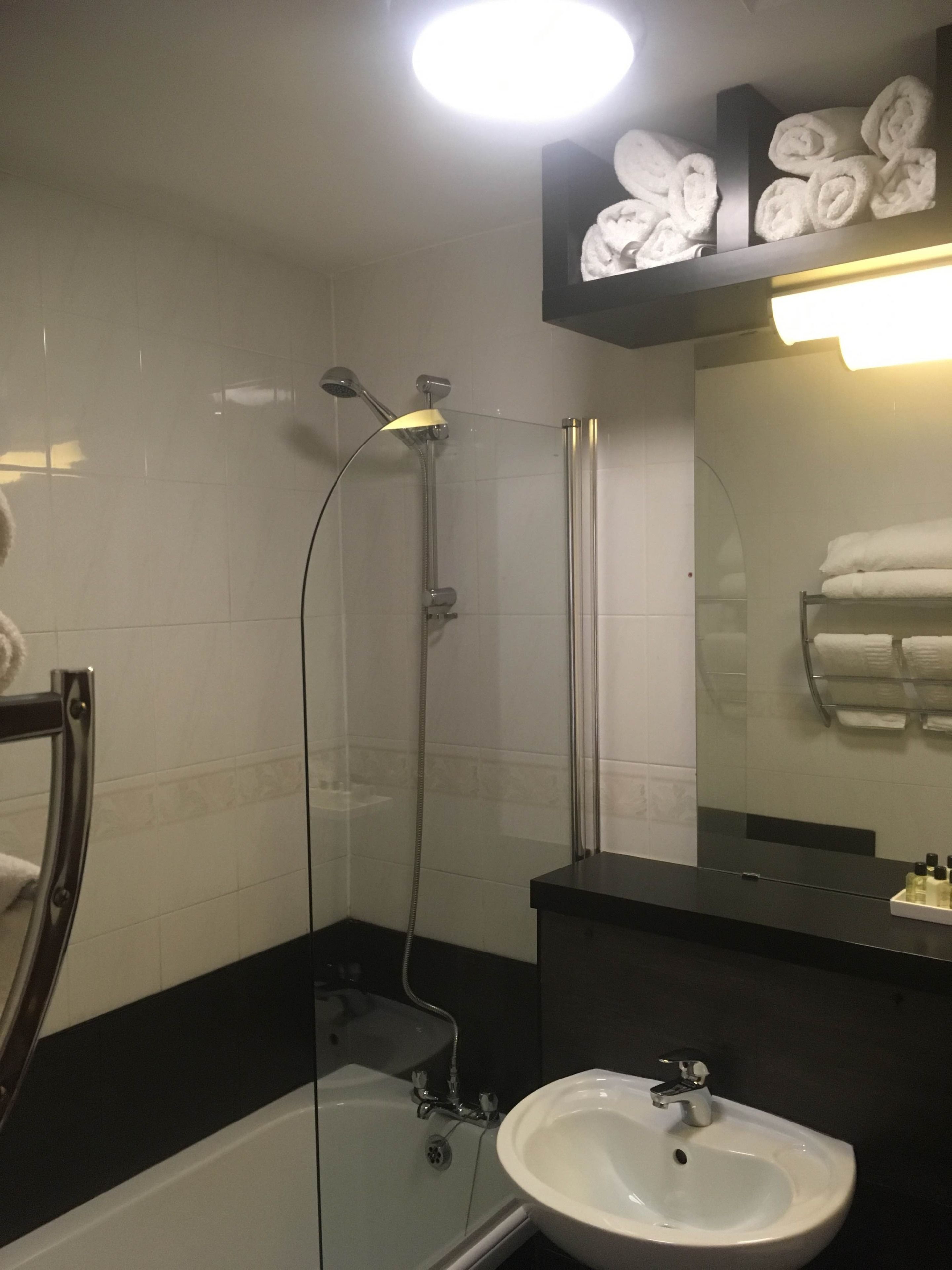 Un baño con ducha envuelta en cristal, bañera, lavamanos y un perchero con toallas dobladas.