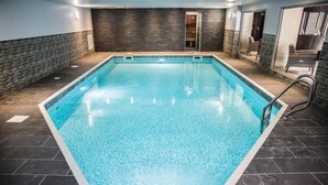 An indoor swimming pool with a clear blue water, surrounded by dark tiled flooring and walls with a textured finish. - Gomersal Park Hotel (Cleckheaton)