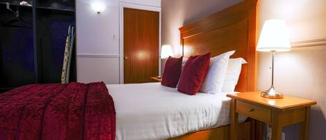 Habitación de hotel con cama, dos lámparas de noche, cabecera de madera y una manta roja.