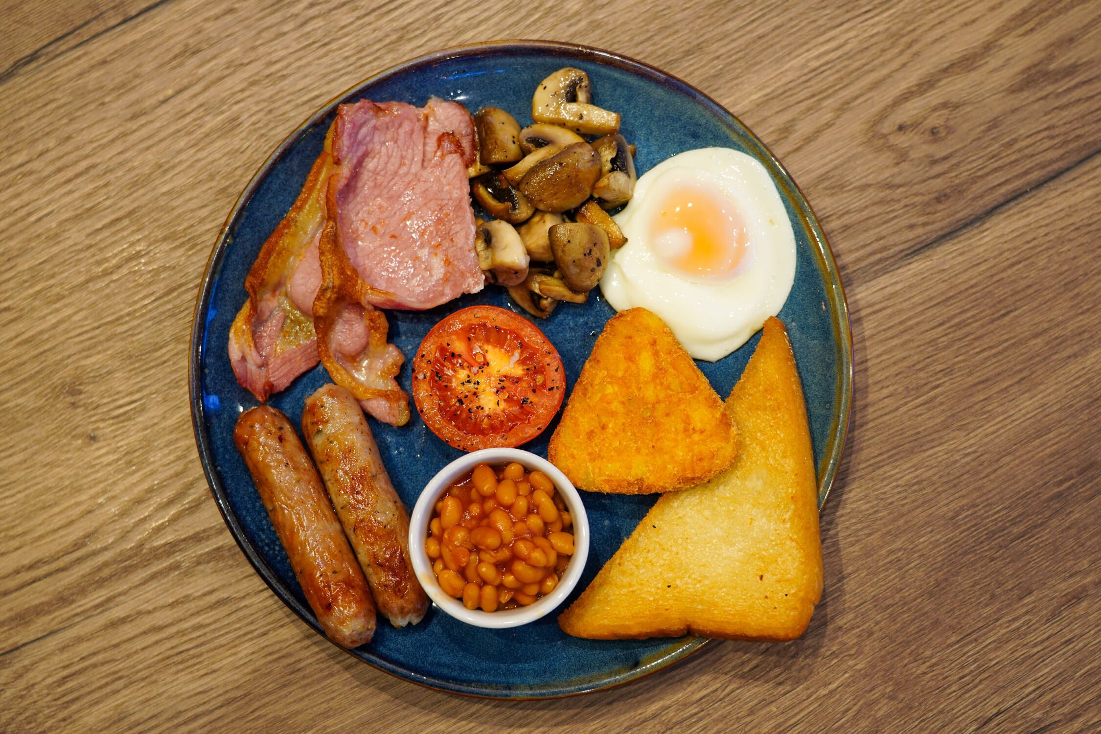 A plate of breakfast food including sausages, bacon, eggs, mushrooms, tomatoes, beans, and toast.