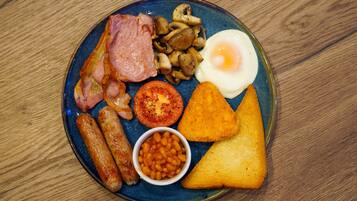 A plate of breakfast food including sausages, bacon, eggs, mushrooms, tomatoes, beans, and toast.