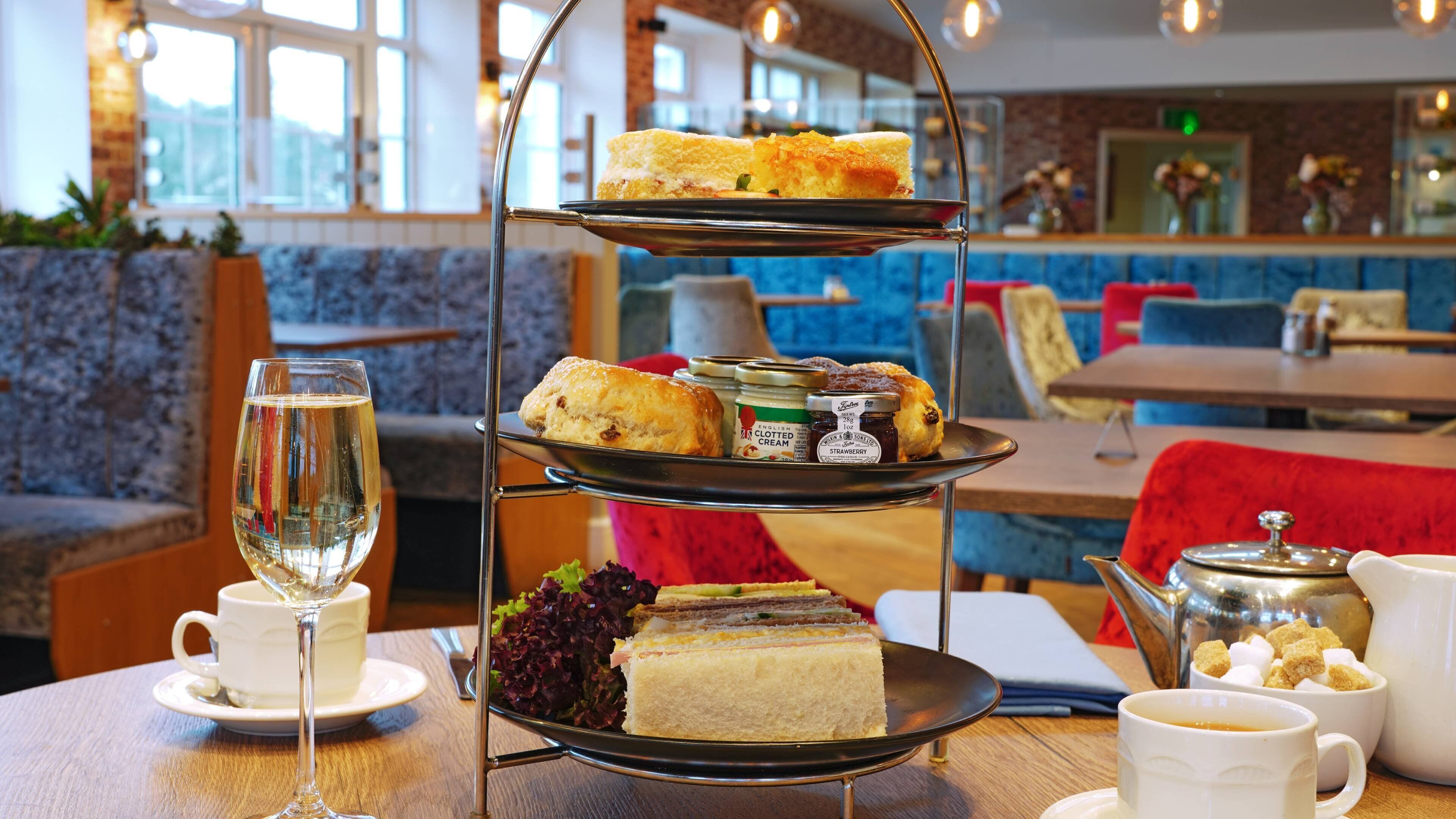A three-tiered dessert stand with sandwiches, scones, and jams in a cafe setting.
