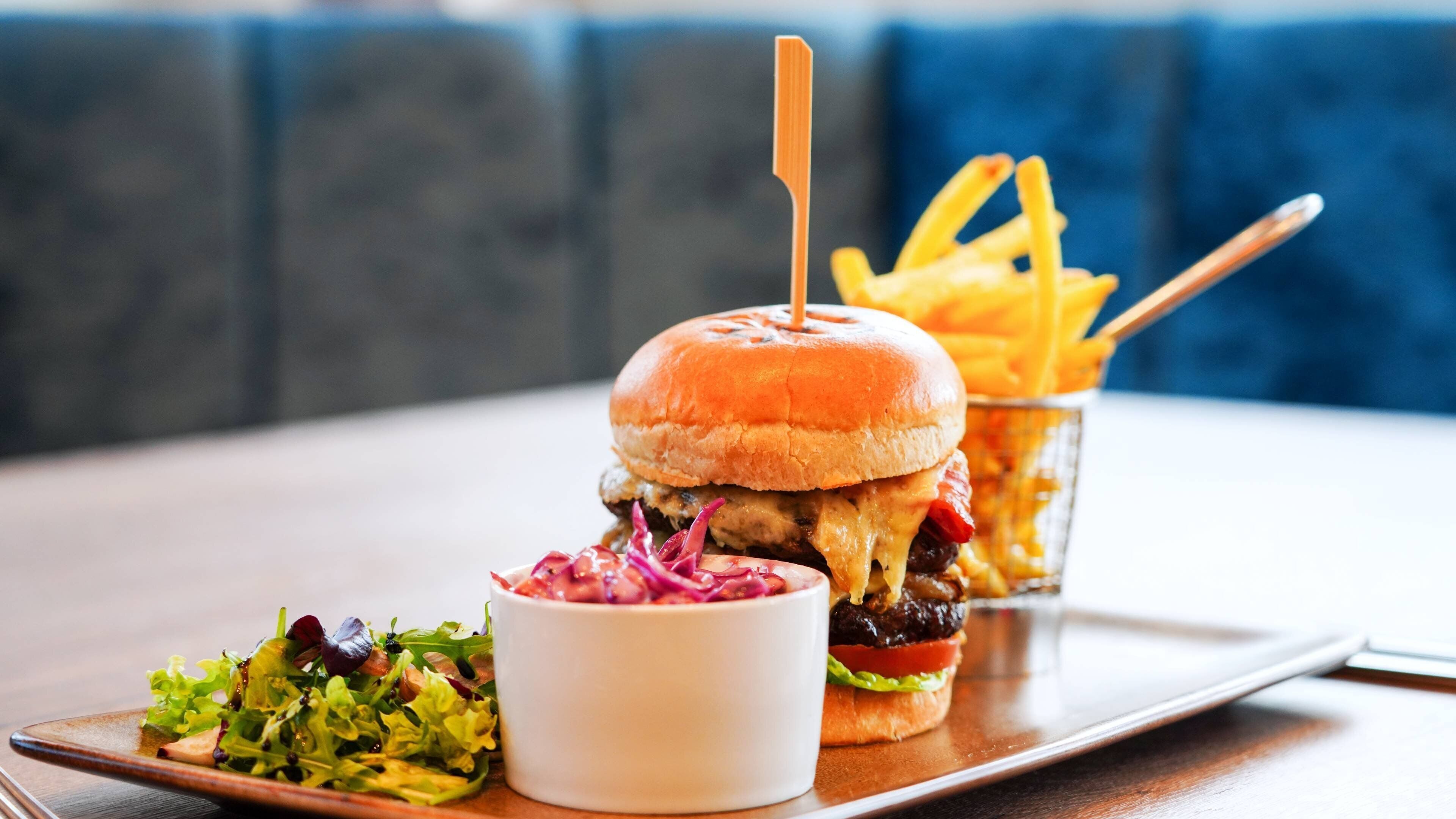 Una hamburguesa con un palillo, papas fritas y una ensalada acompañante en una bandeja.