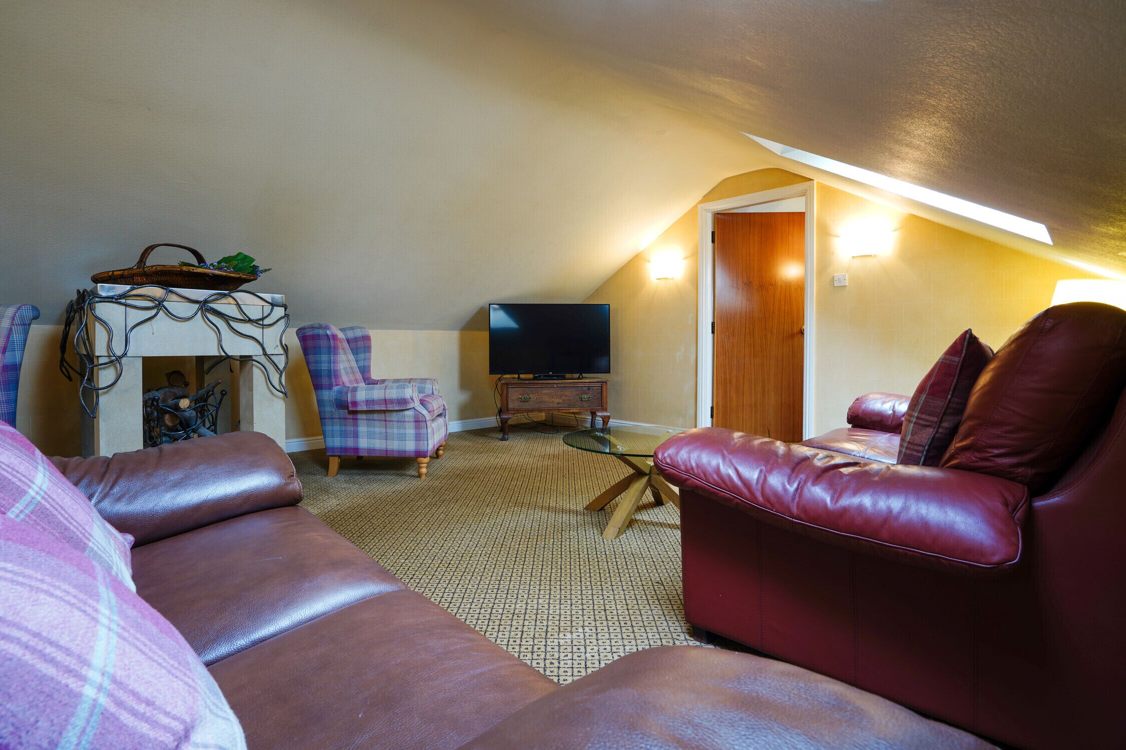 Una sala de estar acogedora con un sofá de cuero rojo, un sillón escocés, una pequeña mesa de madera y un televisor.