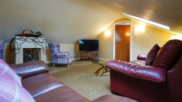Una sala de estar acogedora con un sofá de cuero rojo, un sillón escocés, una pequeña mesa de madera y un televisor.