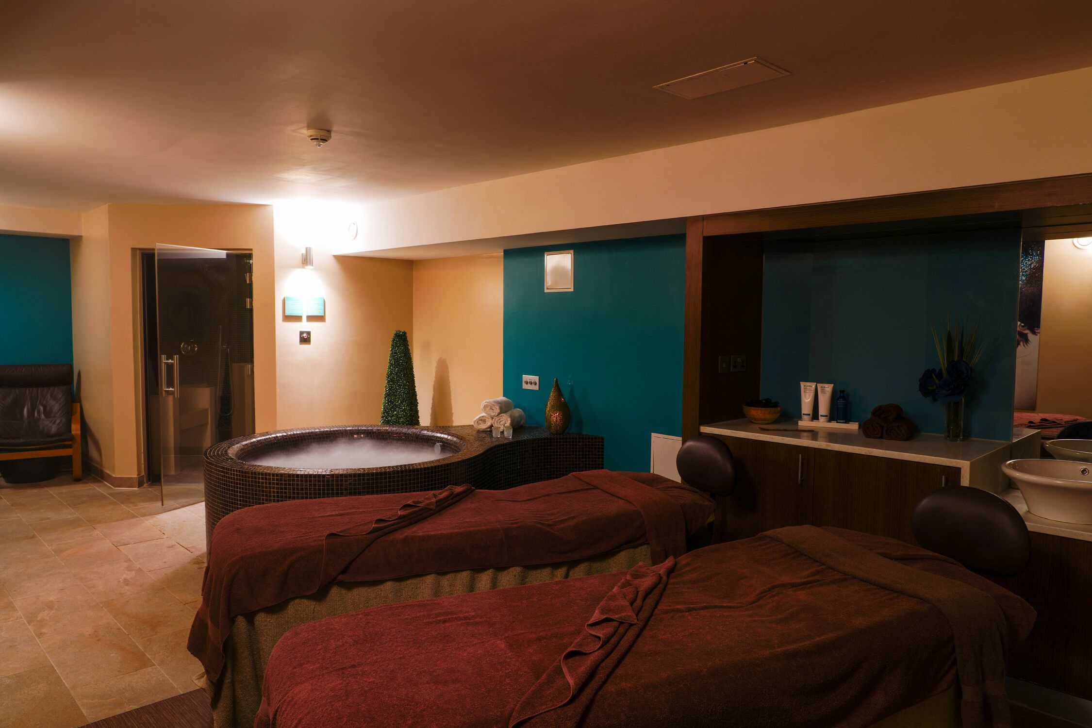 Un cuarto de spa con hidromasaje, dos camillas de masaje, un mostrador de recepción y un espejo.