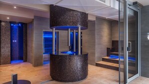 A modern spa area with a circular mosaic water feature, a glass elevator, and a reception desk. - Gomersal Park Hotel (Cleckheaton)