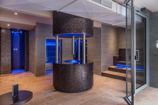 A modern spa area with a circular mosaic water feature, a glass elevator, and a reception desk.