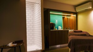 A modern bathroom with a white-tiled shower area, a wooden vanity with a mirror, and a massage table with towels. - Gomersal Park Hotel (Cleckheaton)