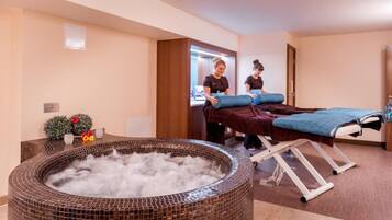 Un cuarto de spa con bañera de hidromasaje, camilla de masaje y dos terapeutas de spa.