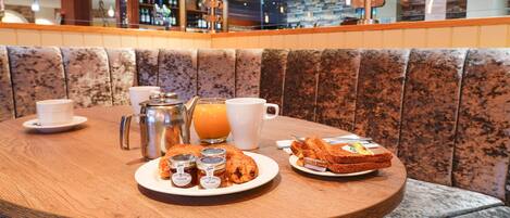 A round wooden table with breakfast items including toast, pastries, and a jug of orange juice.