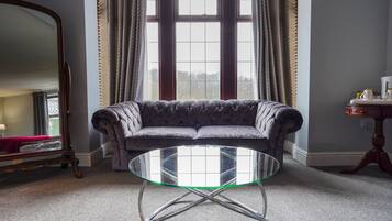 A room with a round glass table, a dark patterned sofa, a wooden side table, and a large mirror.