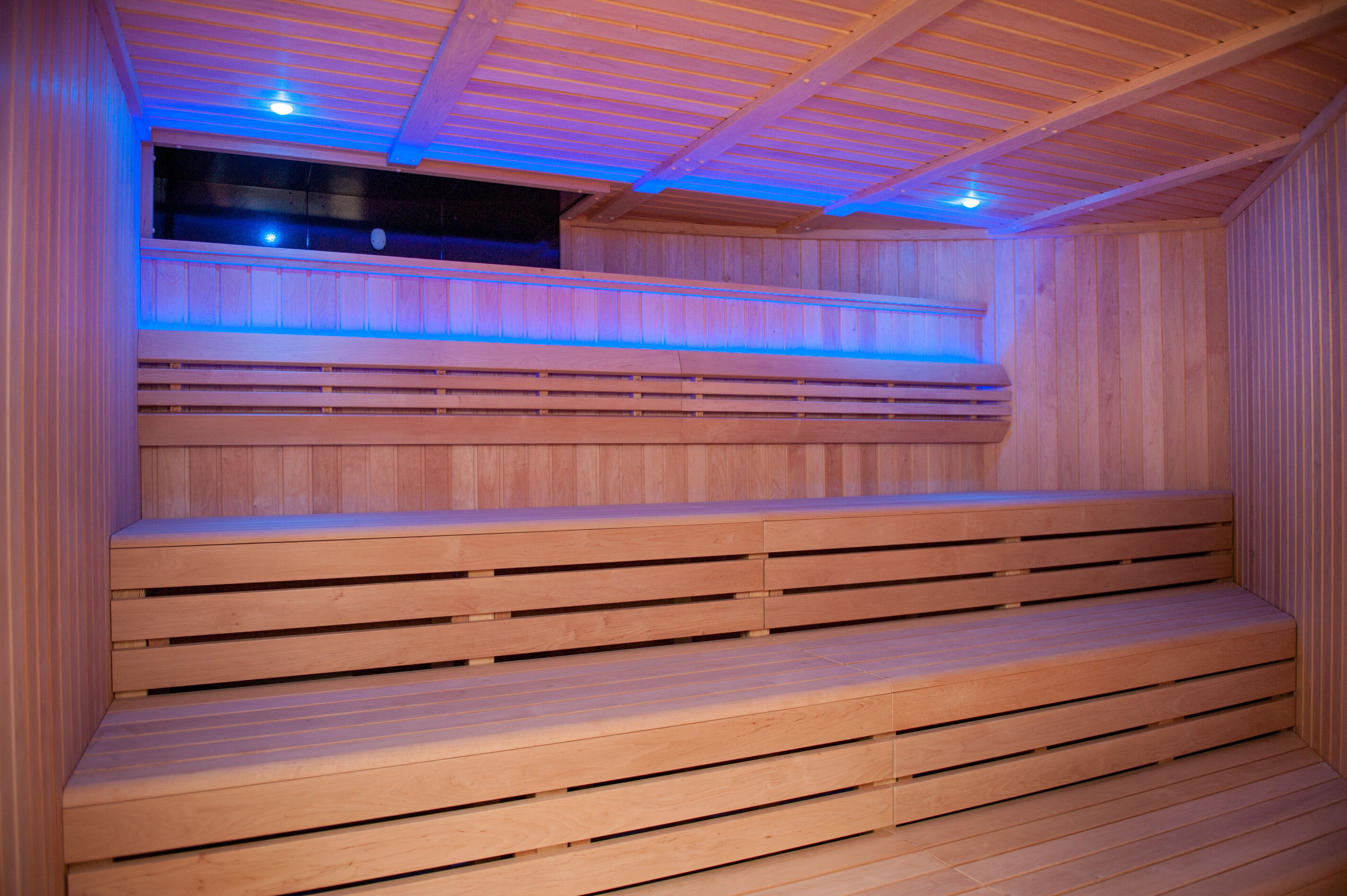 A wooden sauna with tiered seating and blue lighting.