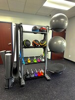 A gym with a rack of kettlebells, medicine balls, and a stationary bike.