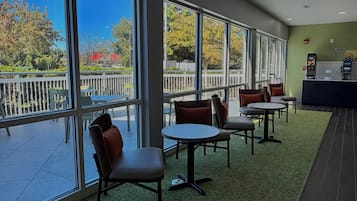 Un área de estar interior con mesas y sillas, ventanas grandes y vistas al exterior.
