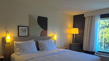 Une chambre d’hôtel avec un grand lit, deux lampes de chevet, un tableau encadré et une fenêtre avec des rideaux.