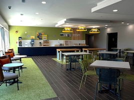 A modern cafe with multiple seating areas, including tables and chairs, and a counter with a menu display.