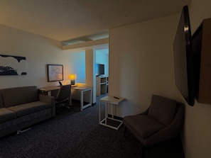 A hotel room with a sofa, a desk, a chair, a TV, and a lamp. - Spark by Hilton Bloomington (Bloomington)