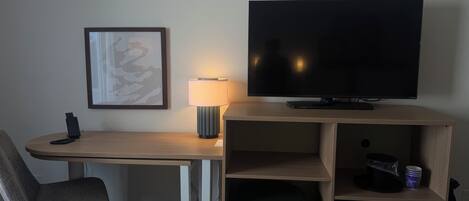 Habitación de hotel con escritorio, silla, televisor, lámpara y cesto de basura.