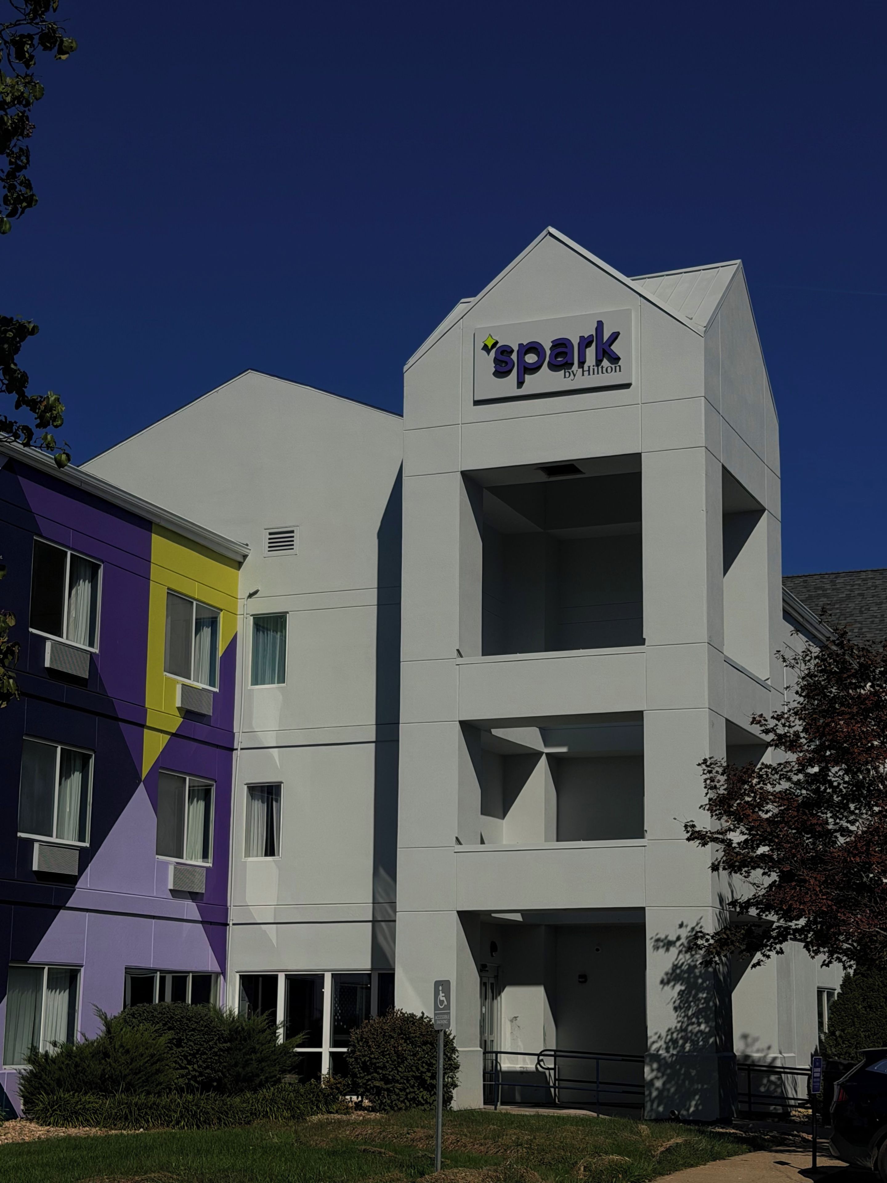 A multi-story building with a 'spark by Hilton' sign, indicating a hotel. It features a modern architectural design with a flat roof and a mix of window styles.