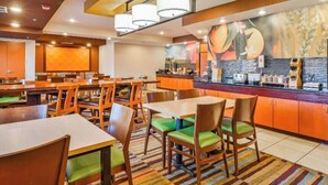 A hotel dining area with multiple tables and chairs, a counter with a coffee machine, and a mural on the wall.