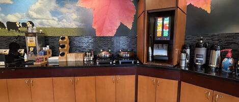 A kitchen area with a coffee machine, a waffle maker, and a mural on the wall.