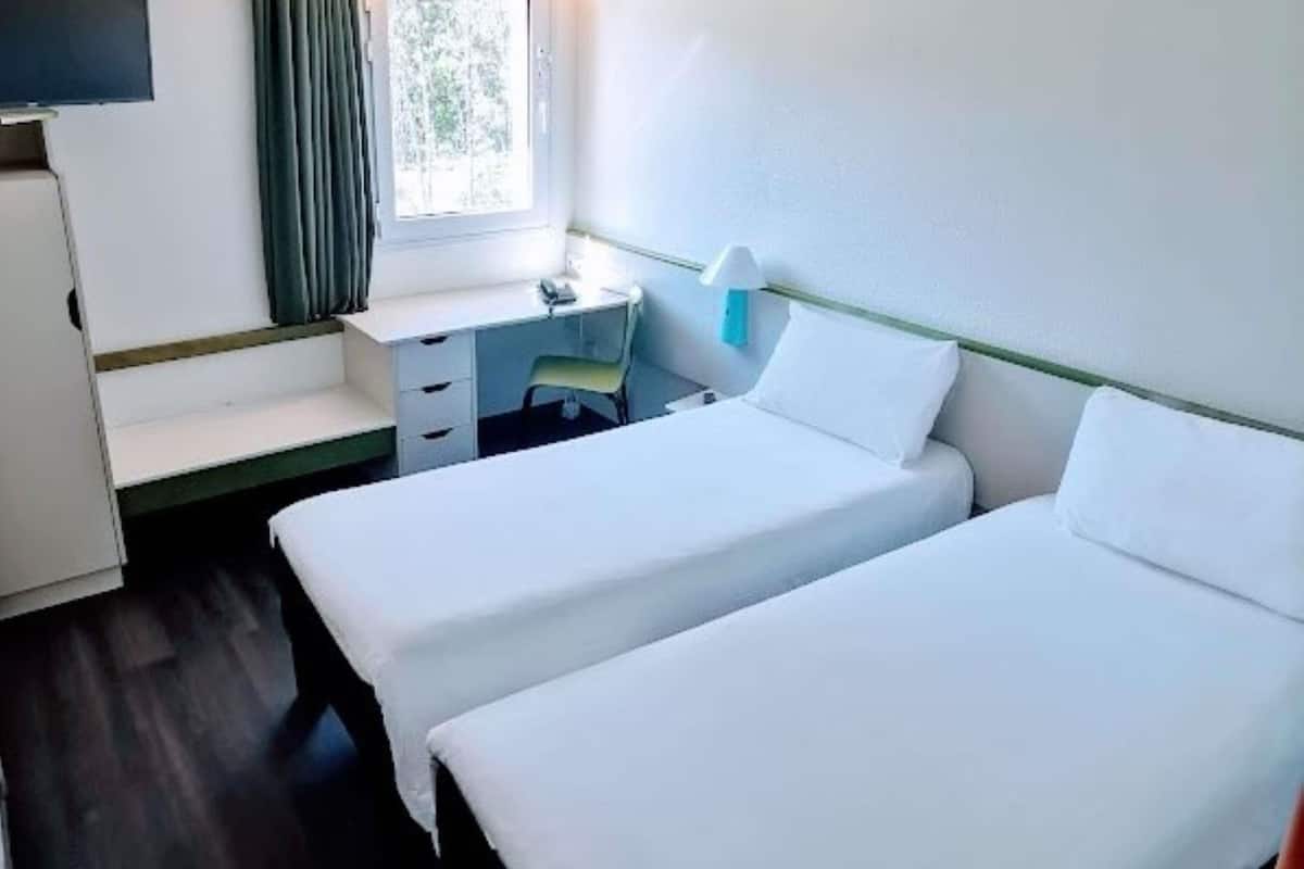 A room with two beds, a desk, a chair, and a window.