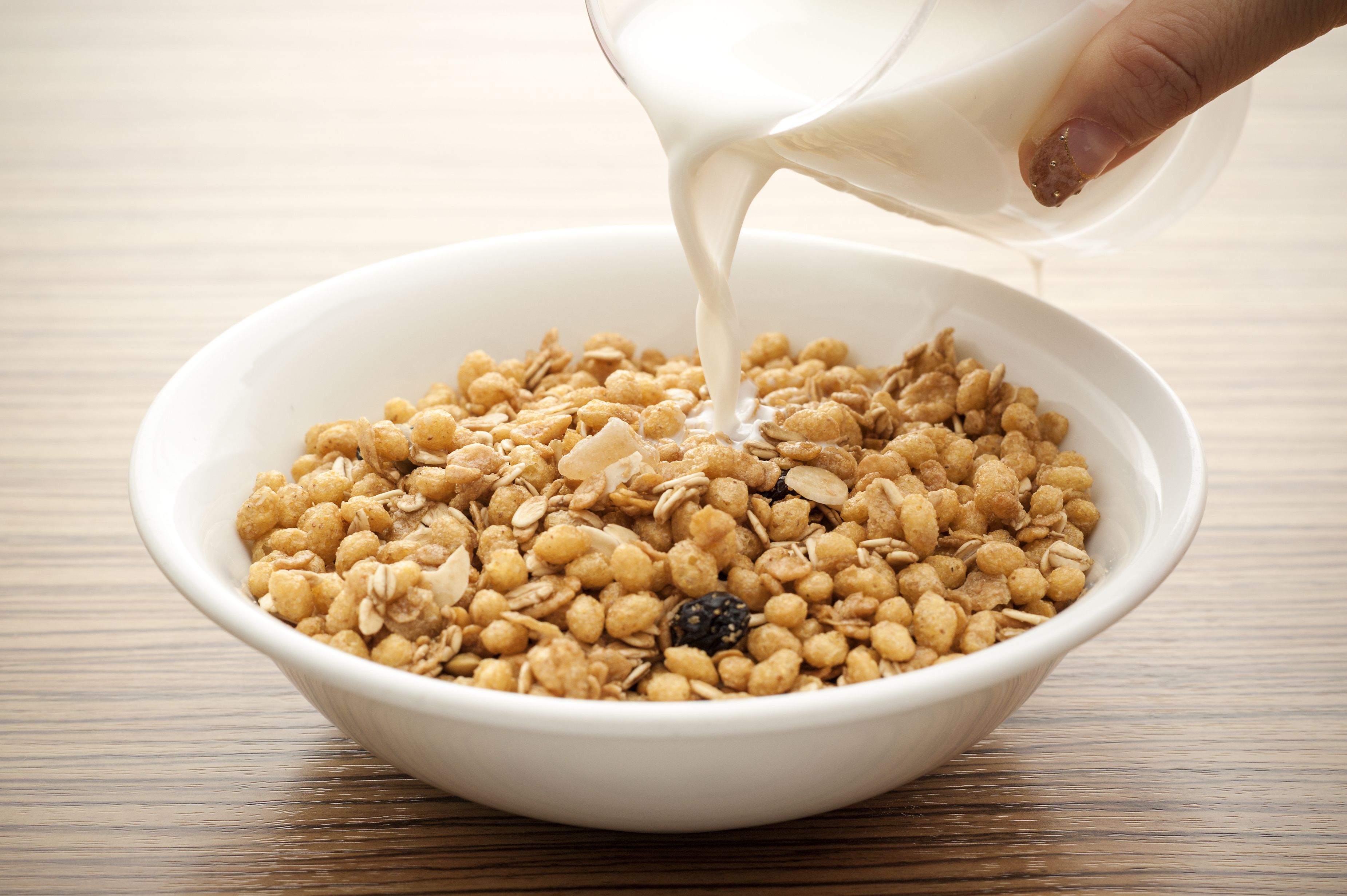 Un tazón blanco lleno de granola y una mano vertiendo leche.
