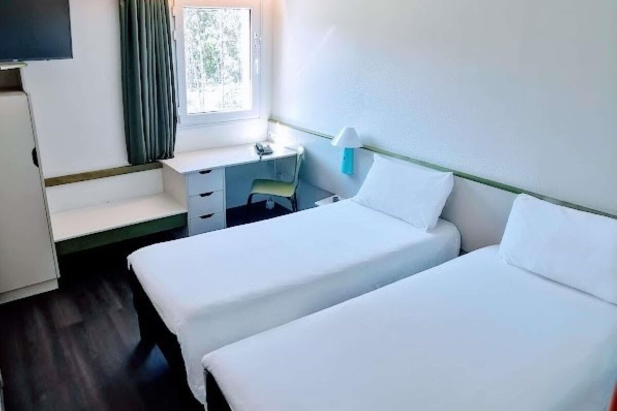 A room with two beds, a desk, a chair, and a window.