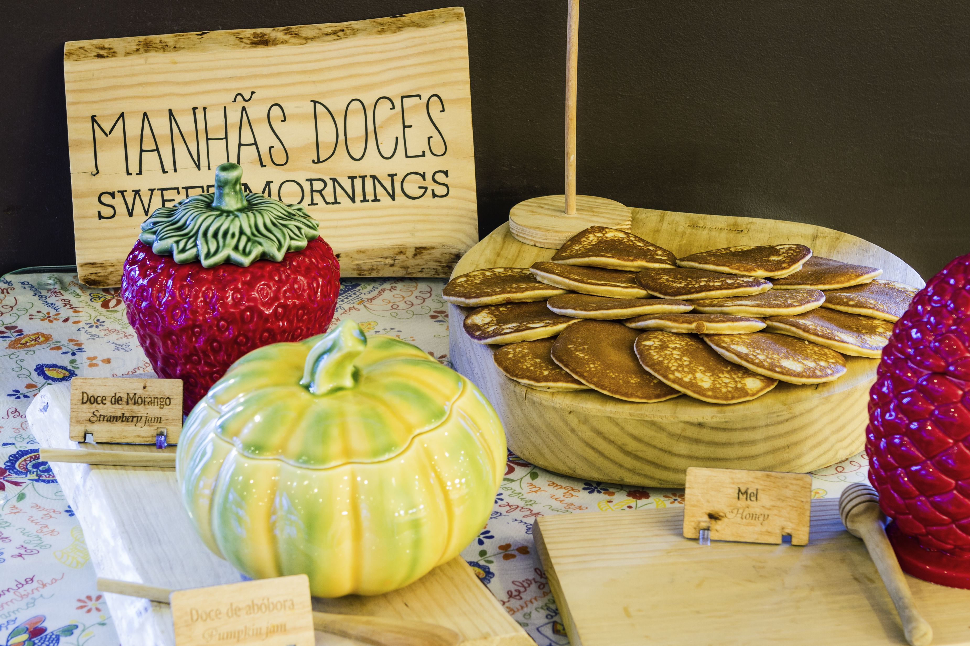 Exposição de itens de pequeno-almoço, incluindo panquecas, doce de morango e doce de abóbora.