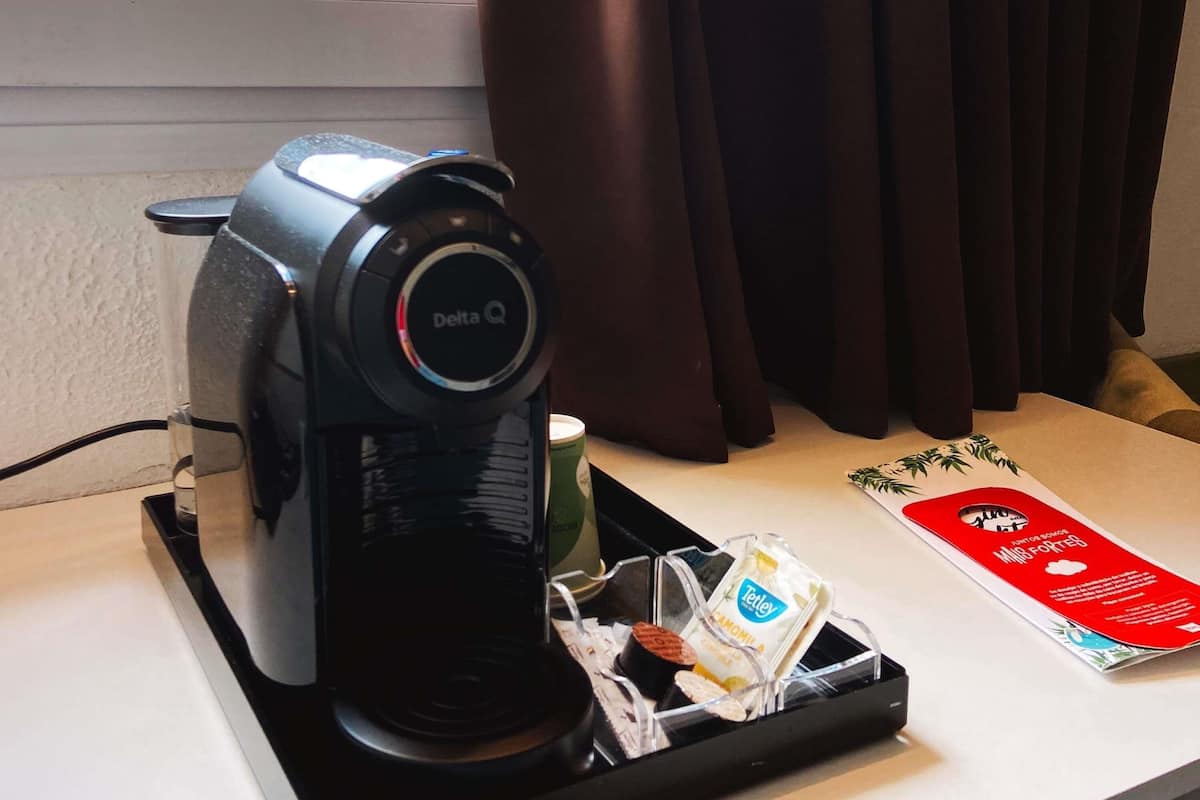 A coffee maker with a 'Delta Q' label, a tray with a coffee cup, a menu, and a small package of Tetley tea.