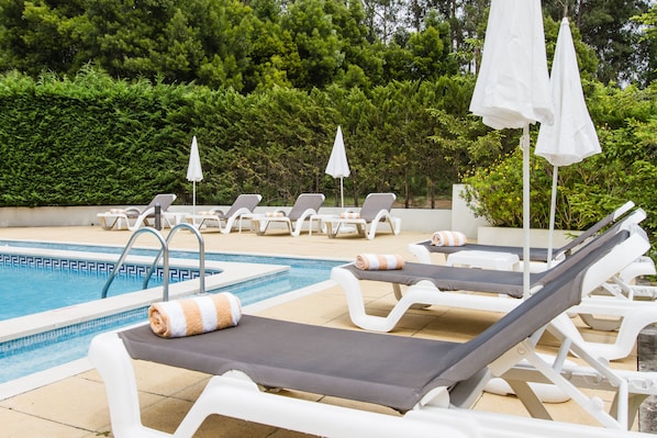 Una piscina al aire libre de temporada, sombrillas, tumbonas