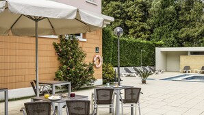 Ein Außenbereich mit Terrasse, Tischen, Stühlen, einem Swimmingpool und einem Rettungsring an einer Wand.