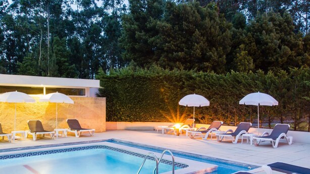Ein Schwimmbecken mit Liegestühlen und Sonnenschirmen, umgeben von einer Hecke und Bäumen.