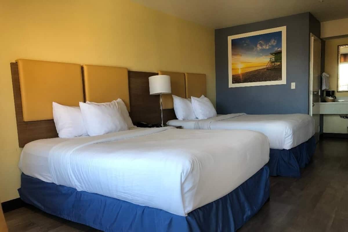 A hotel room with two beds, a nightstand, a lamp, and a painting on the wall.