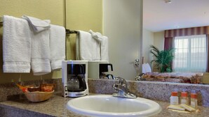 A hotel bathroom with a sink, a coffee maker, a basket of toiletries, and towels hanging on the wall.